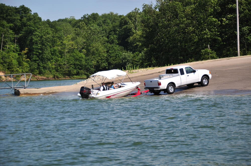 White pickup truck pulling a boat out of the water at the boat launch - best boat insurance.
